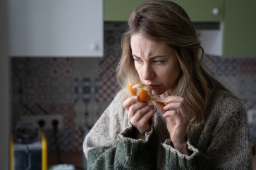 Sick woman trying to sense smell of fresh tangerine orange, has symptoms of Covid-19, corona virus infection - loss of smell and taste, standing at home. One of the main signs of the disease.